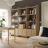 A light wooden LÅDMAKARE storage system against a dark wall. It open shelves and cabinet doors, displaying decor items and books.