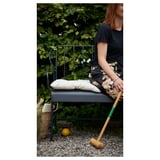 Person sitting on grey LÄCKÖ garden chair with wooden mallet, beside basket on gravel.