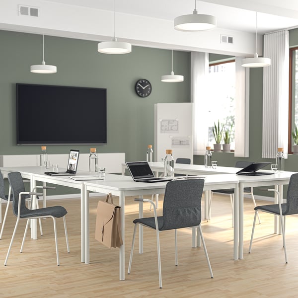 Modern conference room with u-shaped white tables, dark grey LÄKTARE chairs, laptops, bottles, and a large tv on green walls.