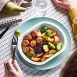 Image a ready-to-eat meal of chicken meatballs, potatoes, brussels sprouts, and gravy in a green bowl with a fork on top.