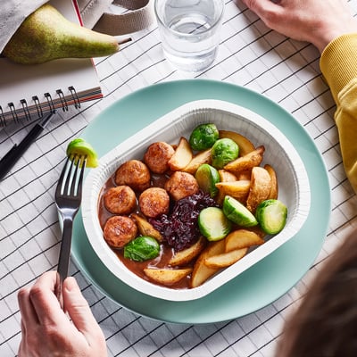 Image a ready-to-eat meal of chicken meatballs, potatoes, brussels sprouts, and gravy in a green bowl with a fork on top.