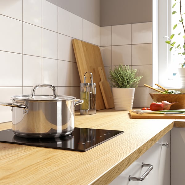 Modern kitchen with stove, wood counter, knives, and plants.