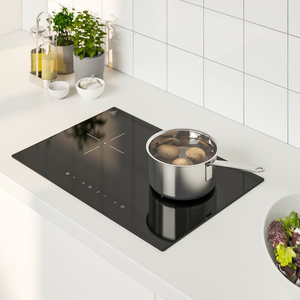 Small black induction stove with pan, surrounded by kitchen items, including bowls, bottles, and salad bowl.