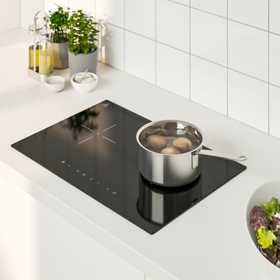 Small black induction stove with pan, surrounded by kitchen items, including bowls, bottles, and salad bowl.