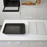 Modern kitchen with oven, baking tray, and wire rack on counter. Oven open, empty.