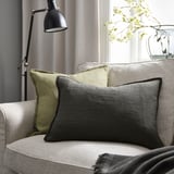 Cozy living room with gray LAGERPOPPEL pillow on beige couch, black lamp, and white flowers.