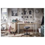 Industrial garage desk setup with LAGKAPTEN table, black stool, wall clutter, bike, and tools.