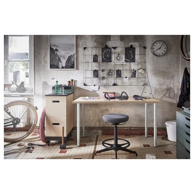 Industrial garage desk setup with LAGKAPTEN table, black stool, wall clutter, bike, and tools.