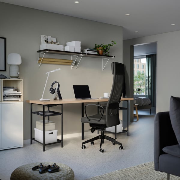 Modern home office with desk, chair, laptop, lamp, headphones, books, plants, cabinet, sofa.
