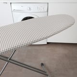 Image shows an ironing board with a new cover featuring a checkered pattern, improving ironing smoothness.