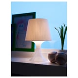 A lamp with a beige shade on a dark shelf, illuminating the area with soft light.