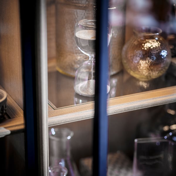 Display shelf with hourglass and glass decor. Blue frame, wooden shelf, vintage design.