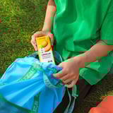 Person holding ikea LÅNGLUR fruit and vegetable smoothie box, sitting on blue mesh bag with green trim.