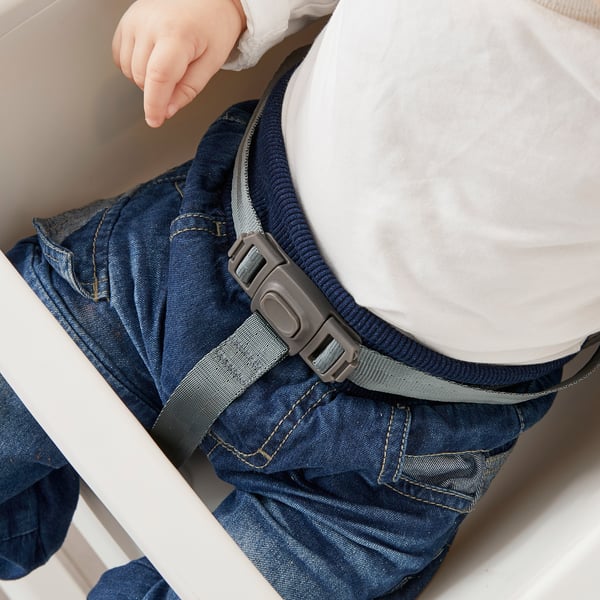 Childs hand reaches out while seated in a highchair. The gray safety belt across the lap ensures security.