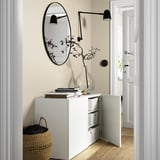 White storage unit with glass doors, mirror, and wall lights. It hides and displays items while offering modern storage.
