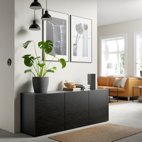 Modern living room with black sideboard, plant, pendant lights, art, and brown sofas by a bright window.