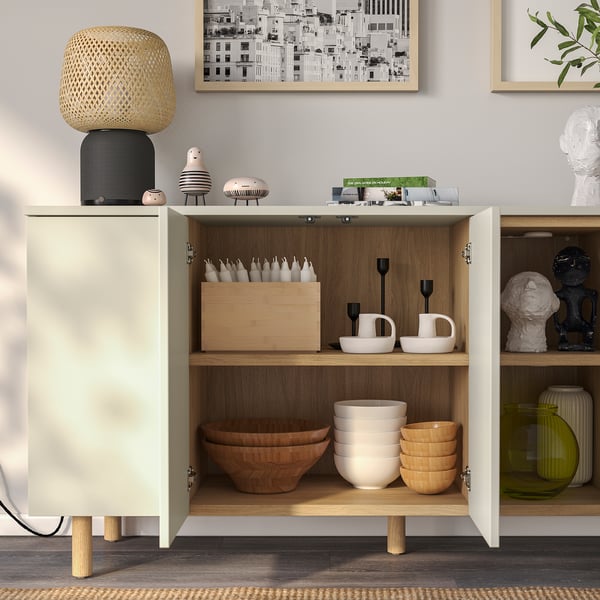 Modern cabinet with open and closed storage. Bowls, cups, and candles neatly organized, with minimalist design and wooden legs.