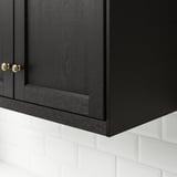 Black kitchen cabinet with gold handles, fitted above white tiles.