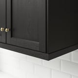 Black wooden cabinet with gold handles. Positioned above white tiled backsplash.