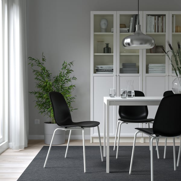Modern dining area with white LIDÅS chairs, gray seat shells, metal legs, under hanging light, black table, bookshelves, plant, and curtained window.