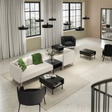 Modern living space with white LILLEHEM sofas, black coffee tables, and black chairs, accented with green throws and decorative plants.