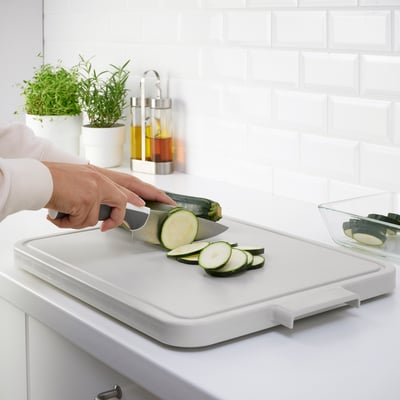 Person slices zucchini on a plastic cutting board over a sink.