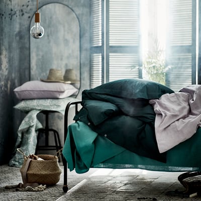 Peaceful bedroom with teal bedding, wicker basket, mirror, and hanging bulb.