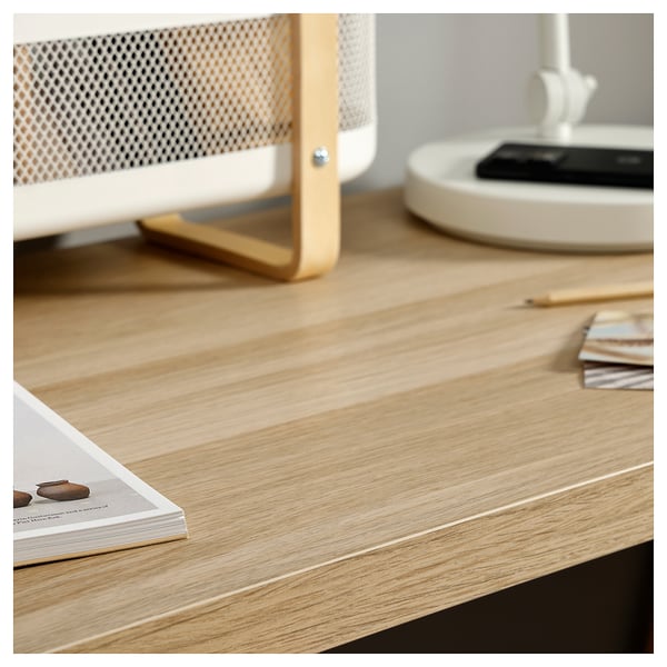 Minimalist desk setup with open magazine, pencils, and white lamp on light wood table.