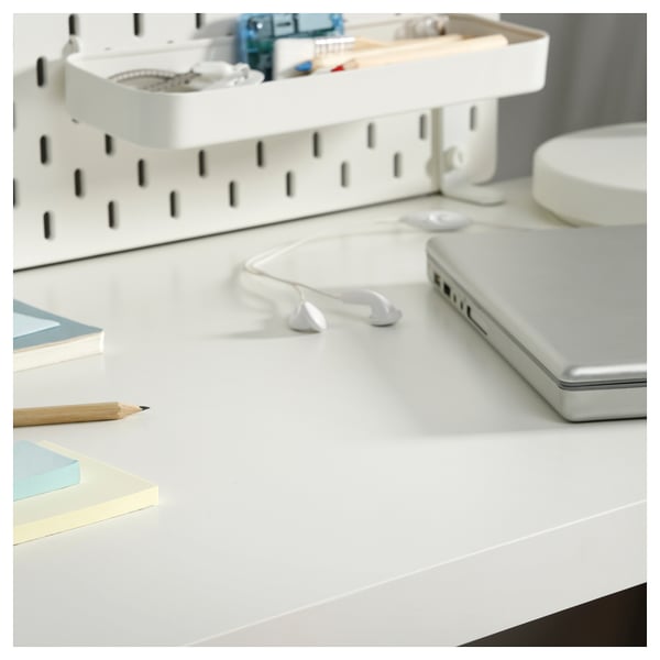 Clean, minimalist white desk setup with laptop, earphones, pencil, and shelves holding various items.