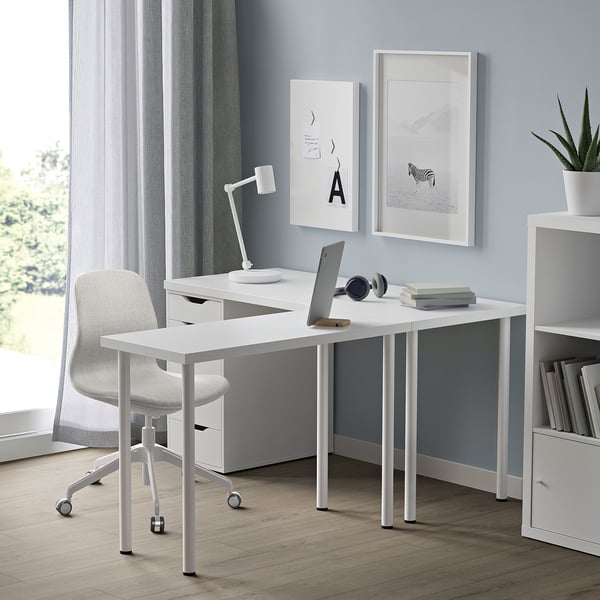 Home office with white LINNMON desk, laptop, chair, and decorations. Compact yet spacious, fitting under wall art and beside shelving.