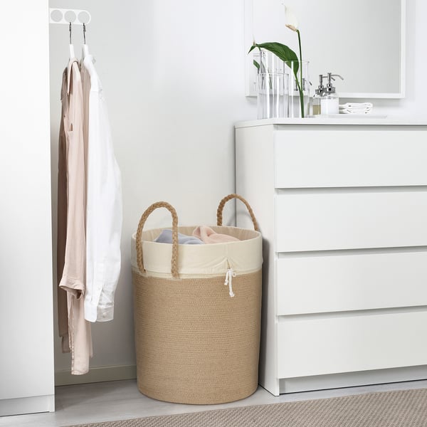 LJUNGAN beige jute laundry basket, large, with handles, near white dresser, holding clothes.