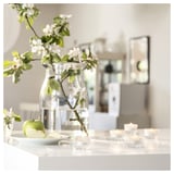 Kitchen counter with a glass vase of white blossoms, green apples, and lit candles.