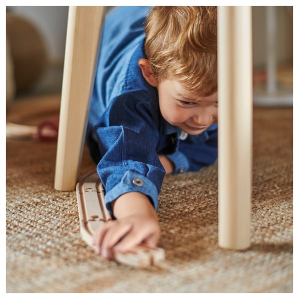 Young boy in blue shirt playing with wooden toy under table with beige rug.