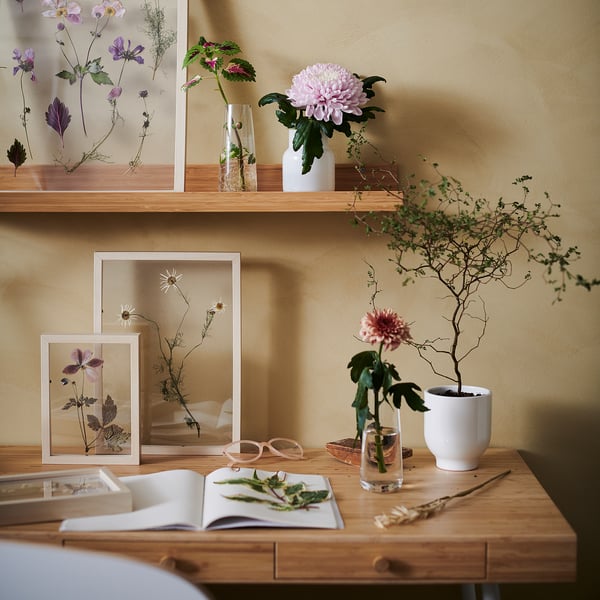 Indoor scene with wooden table, pressed flower art, fresh flowers, nature decor against a warm beige wall.