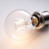 Close-up of glowing, retro light bulb in metallic fixture emitting warm white light.