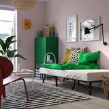 Modern living area with a foldable bed, green cabinet, patterned rug, and cozy pillows.