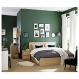 Modern bedroom with green walls, light wood furniture, gray bedding, black lamps, white curtains, and wall art.