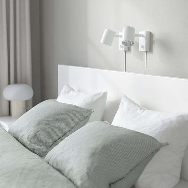 White minimalist bedroom with MALM bed, green blanket, wall & nightstand lamps.
