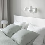 White minimalist bedroom with MALM bed, green blanket, wall & nightstand lamps.