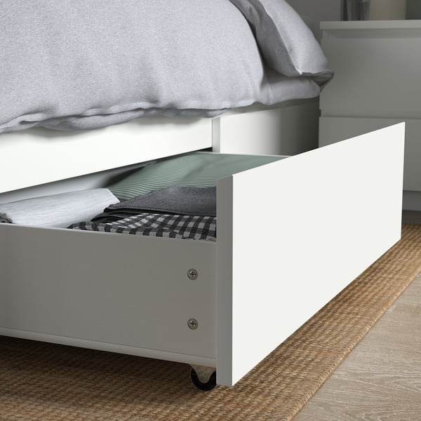 Bed with open drawer showing folded clothes, under white bed frame.