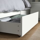 Bed with open drawer showing folded clothes, under white bed frame.