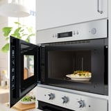 A stainless steel microwave with a meal inside, placed above a stove, set at 11:30. The microwave door is slightly ajar.