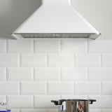 A sleek, white range hood with a metallic grease filter, mounted on a white tiled wall, featuring modern design and utility.