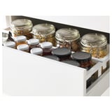 White kitchen drawer fully extended, holding multiple jars with lids, showcasing organized storage.