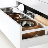 White kitchen drawer fully extended, displaying organized containers: two stainless steel bowls, two wooden bowls, and a wooden cutting board.