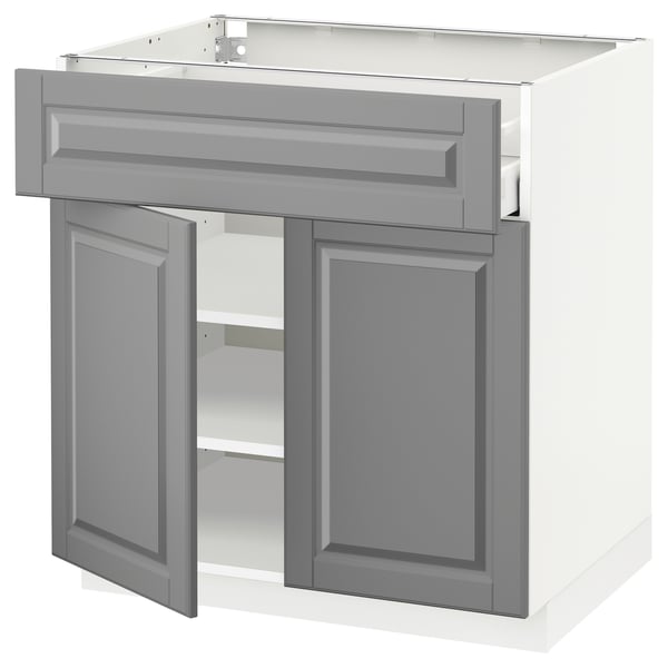 Gray kitchen cabinet with open doors. Beveled edges, metal hinges, and wooden shelves. Traditional style.