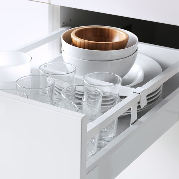White kitchen drawer with glasses, a white bowl, and plates organized neatly.