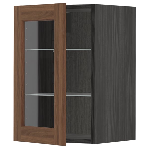 A METOD kitchen cabinet with walnut-finished glass doors and dark frame, featuring adjustable shelves.