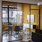 Modern meeting room with MITTZON yellow table, grey chairs, plants, and tv on wall.