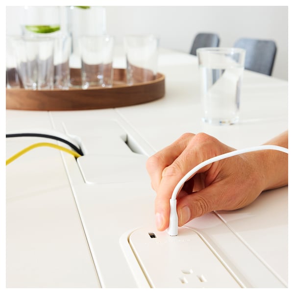 Hand connects white cord with plug to sleek, modern high table with cable management.